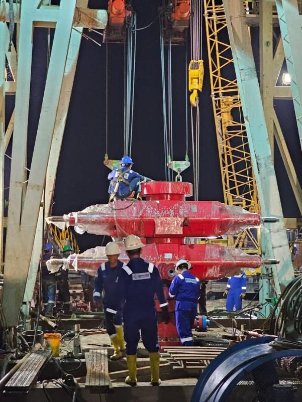 Field crew guiding a red wellhead assembly under a crane hook